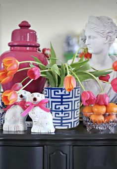 vases with tulips and other flowers sit on a black dresser in front of a busturine