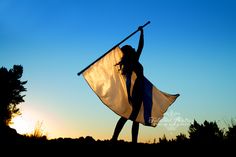 a woman holding a white and blue flag in the air with her hands up at sunset