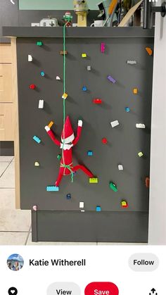 an elf hanging from a bulletin board with legos on it's back wall