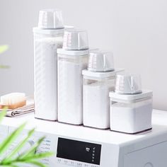 five white containers sitting on top of a dryer in front of a green plant