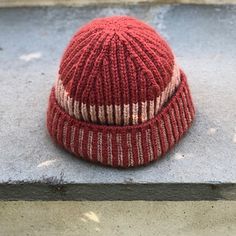 a red and white knitted hat sitting on the ground next to a cement wall