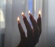 two hands holding lit matchsticks in front of a window