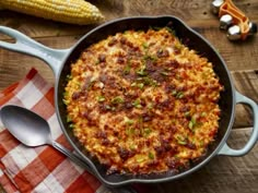 a skillet filled with food sitting on top of a wooden table next to corn