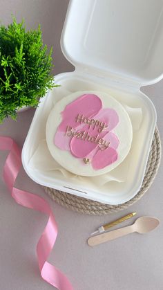 a birthday cake in a white box with pink hearts on it next to a green plant