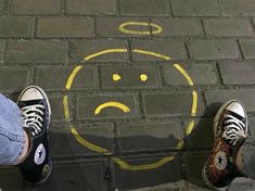 two people standing in front of a smiley face drawn on the sidewalk with yellow paint