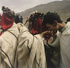 a group of people standing around each other with head coverings on their heads and in the background are mountains