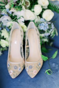 the bride's wedding shoes are sitting next to a bouquet of white and blue flowers