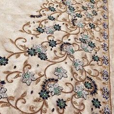 an embroidered fabric with blue and green flowers on the bottom, along with gold thread