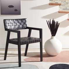 a white vase sitting next to a black chair in a living room on top of a rug