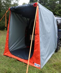 an orange and blue tent with the door open in a grassy field next to trees