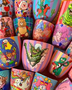 there are many different colored cups on the table with cartoon characters painted on each one