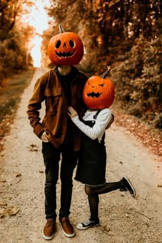 two people standing on a dirt road with pumpkins on their heads and one holding the other's head