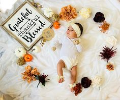 a baby laying on top of a white blanket next to pumpkins and flowers in front of a sign that says grateful