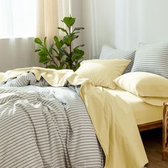 a bed with yellow sheets and pillows in a bedroom next to a plant on the floor