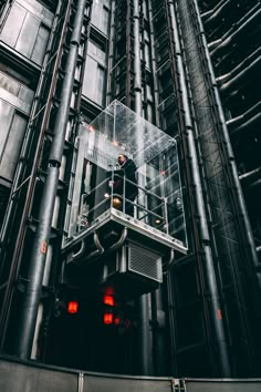 a man standing on top of a glass box in front of a tall building with pipes