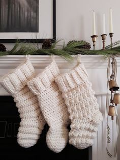 two crocheted christmas stockings hanging from a mantel with candles and pine cones