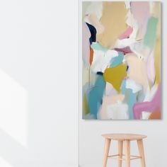 an abstract painting hangs on the wall next to a stool in a room with white walls