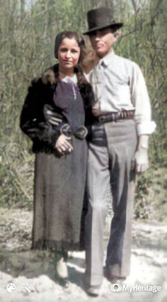 an old photo of a man and woman standing next to each other in the woods