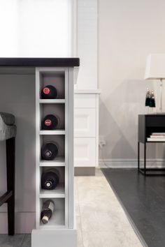 a white shelf filled with wine bottles next to a black and white chair in a room