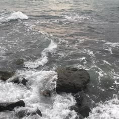 the water is choppy and there are rocks in the foreground with waves coming up on it