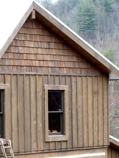 a small wooden cabin with two windows and a bench on the porch next to it