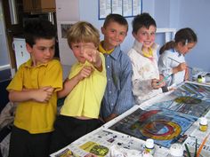 several children are standing around a table with magazines on it and paintbrushes in front of them