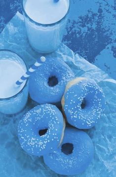 blue doughnuts and two glasses of milk are on the table next to each other