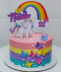 a birthday cake with a unicorn on top and rainbow decorations around the edges, sitting on a white table