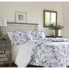 a bed with blue and white comforters in a room next to a dresser, mirror and lamp