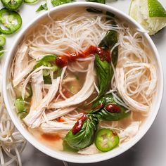 a white bowl filled with chicken noodle soup next to sliced jalapenos