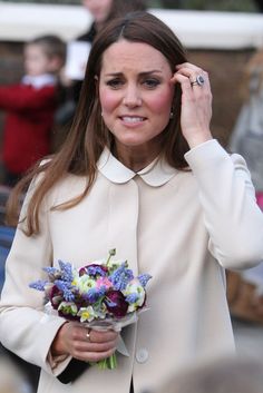 a woman in a white coat holding a bouquet of flowers and talking on the phone