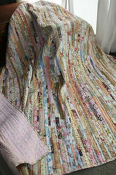 a bed with a colorful quilt on top of it next to a white curtain and window