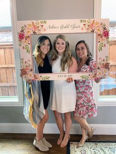 three women pose for a photo in front of a floral frame with the word bride and groom written on it