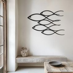 a metal fish sculpture on the wall next to a wooden table and bench in a living room