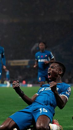 a soccer player is laying on the ground with his mouth open and two other players in the background