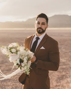 a man in a brown suit holding a white bouquet and looking off into the distance