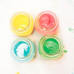 three jars filled with different colored paint on top of a white table covered in confetti and sprinkles