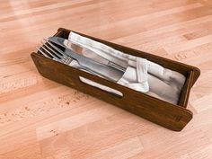 an open wooden box with silverware in it on a wood floor next to a knife and fork