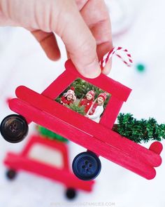 a hand holding a red toy car with christmas decorations on it's side and a small tree in the back