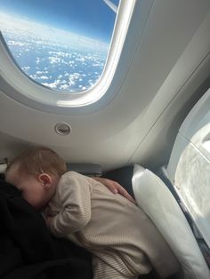 a baby is sleeping on an airplane seat with the view of the sky and clouds