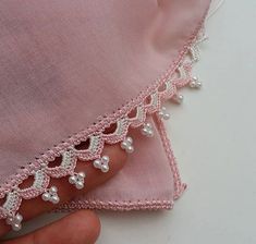 a hand is holding a piece of pink fabric with white beads and pearls on it