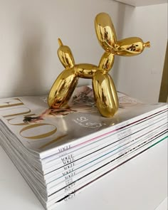 a gold balloon dog sitting on top of a stack of magazines