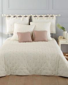 a white bed with two pillows on top of it and some pink pillow cases in the corner