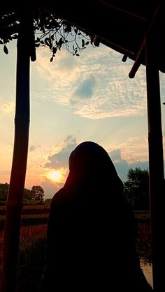 a person standing under a covered structure with the sun setting in the distance behind them