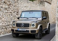 a mercedes benz g - class is parked in front of a stone wall and cobblestone street