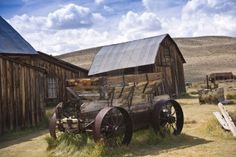 an old car is parked in front of a barn and other farm equipment on the grass