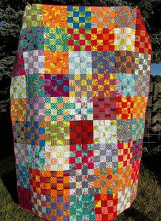 a colorful patchwork quilt is hanging on a wire fence in the grass with trees behind it