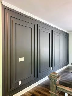 an empty room with wooden flooring and black painted cabinets on the wall, along with a bench