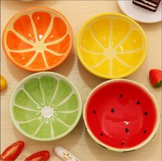 four colorful bowls with slices of orange, lime, and strawberry on the table next to utensils