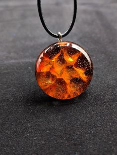 an orange and black glass pendant is sitting on a table with a black cord around it